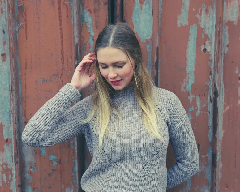 junge blonde frau posiert für die kamera vor rustikaler wand