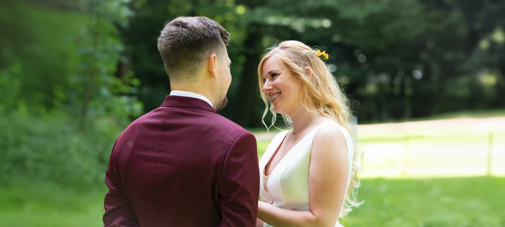 Hochzeitspaar draußen im Grünen sieht sich verliebt an.